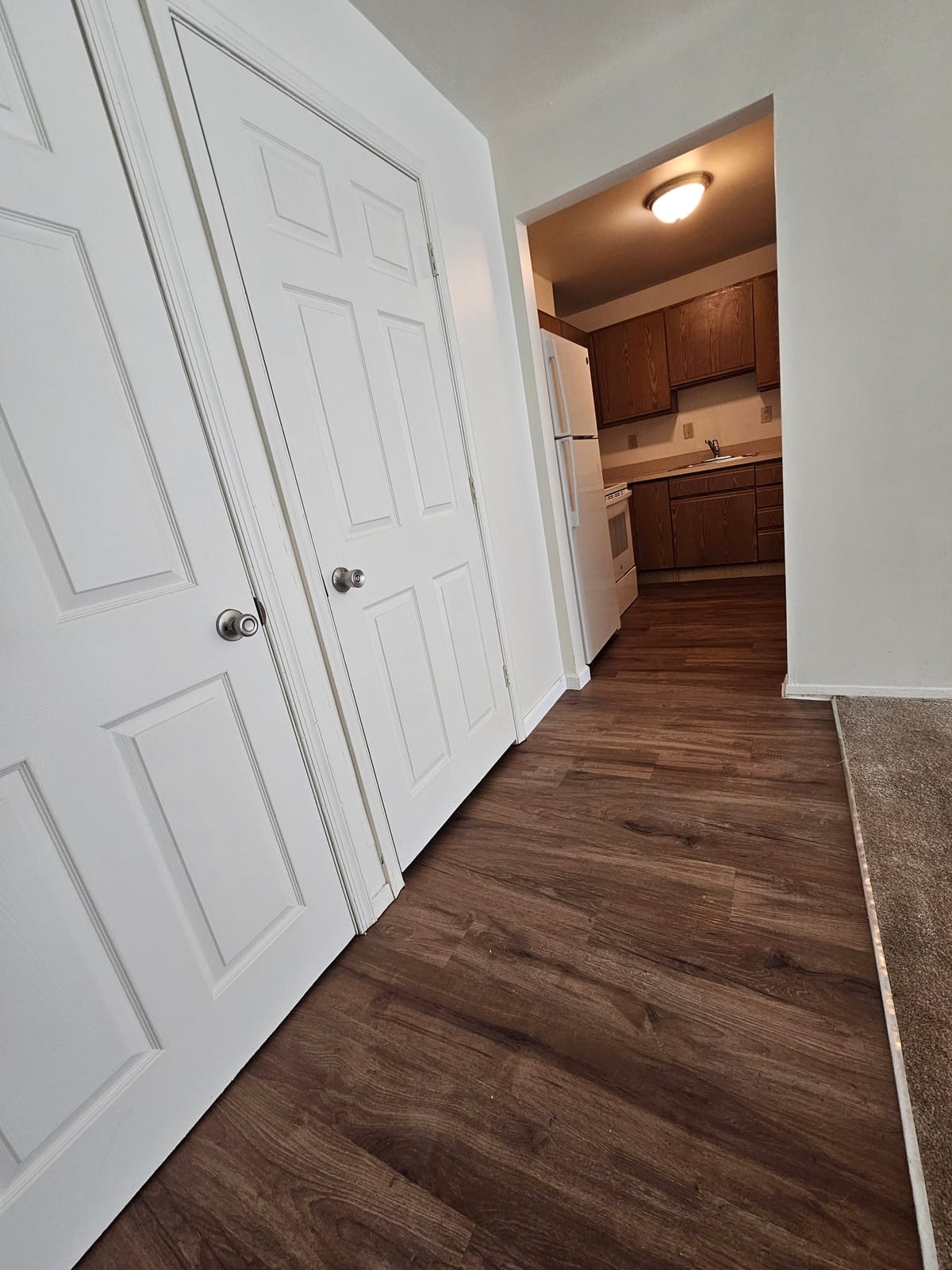 The entry of an apartment at Village Green Apartments, with white closet doors and plank flooring leading to the kitchen